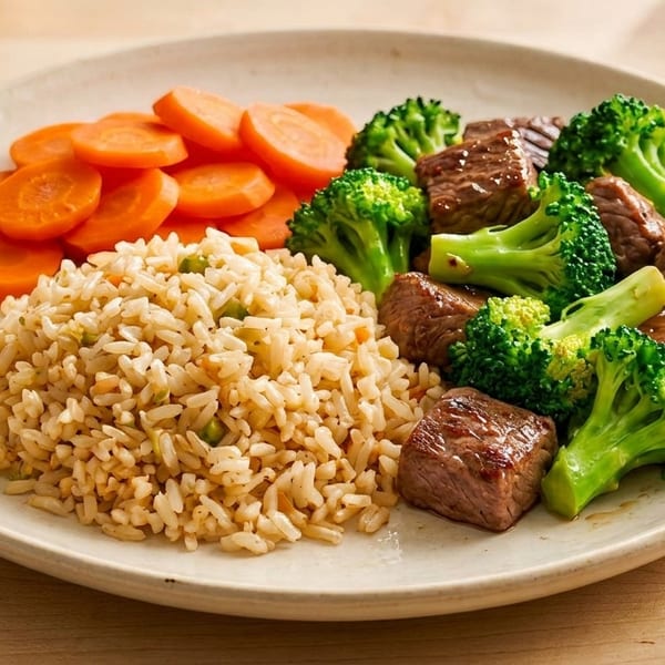 A plate of beef and broccoli with a side of brown rice and sliced carrots.