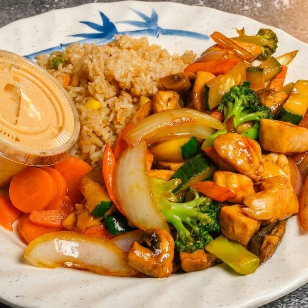 Chicken stir-fry with broccoli, zucchini, onions, carrots, mushrooms, fried rice, and a side of sauce.