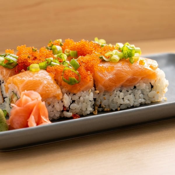 Salmon sushi rolls topped with bright orange roe and green onions, served with wasabi and ginger.
