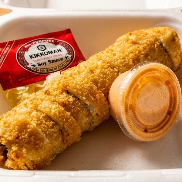 Crispy fried sushi roll with soy sauce packet and spicy mayo in a white takeout container.